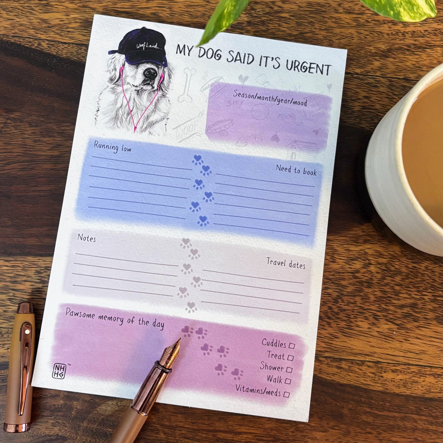A dog-themed daily planner notepad titled 'MY DOG SAID IT'S URGENT' with pastel purple and blue sections, placed on a wooden table next to a pen, coffee cup, and green plant leaves.