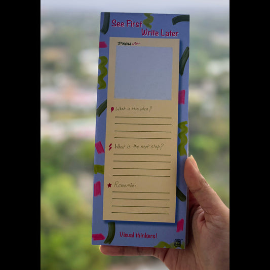 A hand holding a blue and pink 'See First Write Later' sticky note pad with a blank writing area and lined prompts, set against a blurred outdoor background.